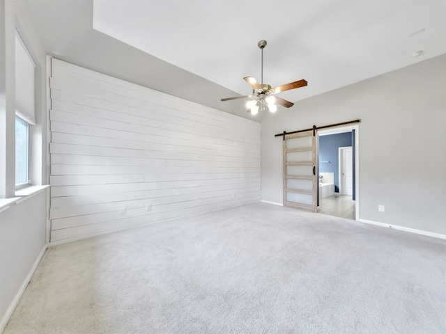 spare room featuring a barn door, wooden walls, light colored carpet, and ceiling fan