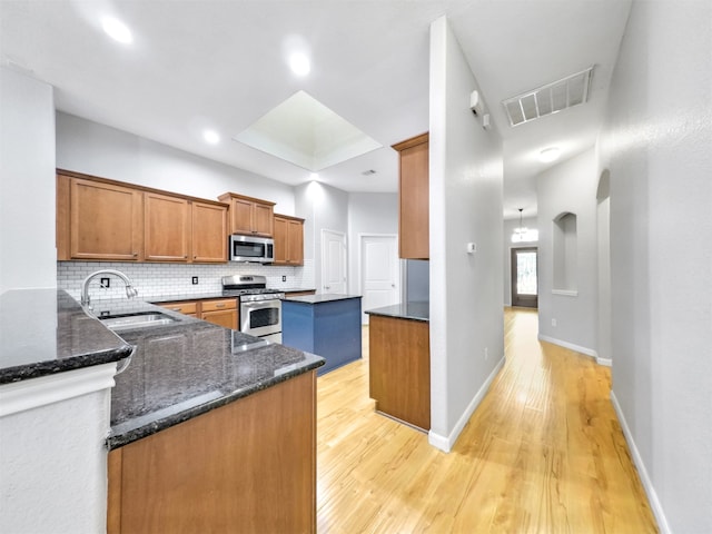 kitchen with sink, tasteful backsplash, appliances with stainless steel finishes, kitchen peninsula, and dark stone counters