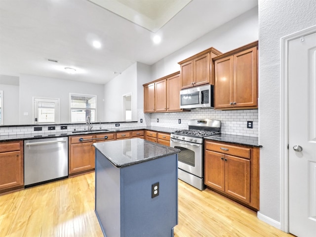 kitchen with a kitchen island, dark stone countertops, decorative backsplash, stainless steel appliances, and light wood-type flooring