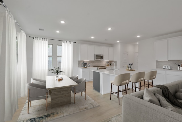 kitchen with a kitchen island with sink, white cabinetry, a kitchen breakfast bar, and appliances with stainless steel finishes