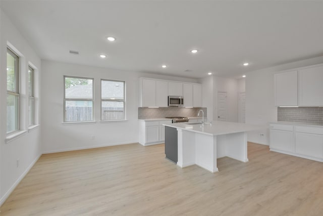 kitchen with light hardwood / wood-style flooring, an island with sink, white cabinets, and appliances with stainless steel finishes