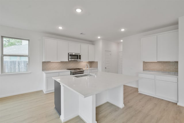 kitchen with white cabinetry, stainless steel appliances, sink, and a center island with sink