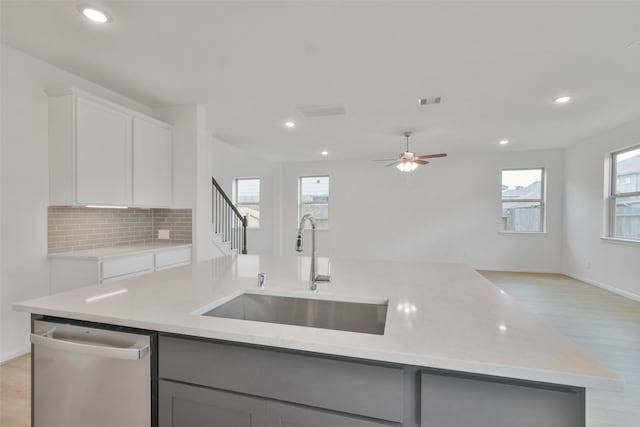 kitchen featuring white cabinetry, sink, backsplash, stainless steel dishwasher, and a center island with sink