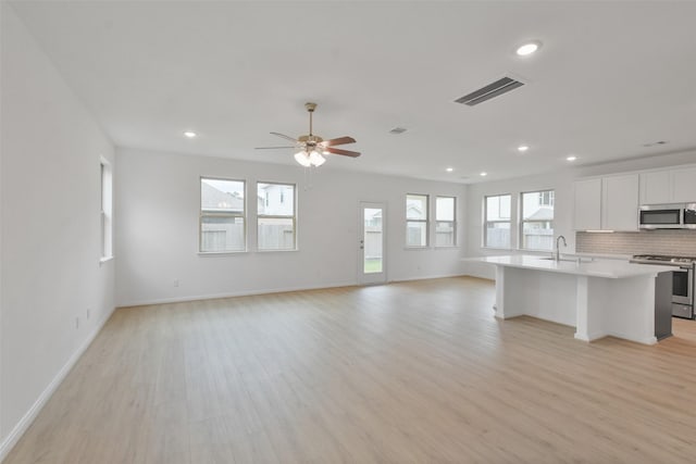 unfurnished living room featuring sink, plenty of natural light, light hardwood / wood-style floors, and ceiling fan