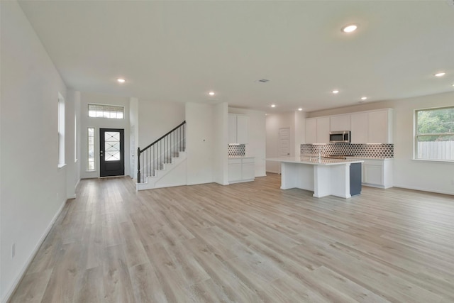 kitchen featuring a kitchen island with sink, backsplash, white cabinetry, and a healthy amount of sunlight