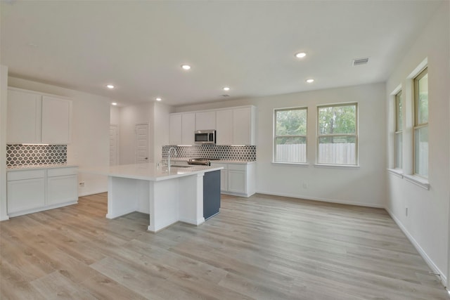 kitchen with tasteful backsplash, a kitchen island with sink, white cabinets, and light hardwood / wood-style floors