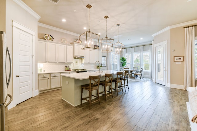 kitchen with a breakfast bar, decorative backsplash, hanging light fixtures, a kitchen island with sink, and stainless steel appliances