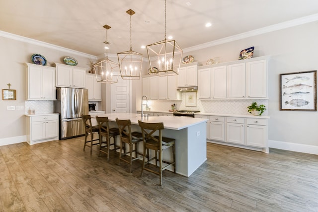 kitchen with stainless steel appliances, an island with sink, hanging light fixtures, and white cabinets