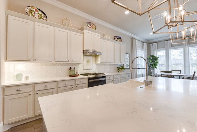 kitchen featuring gas stove, light stone counters, white cabinetry, decorative light fixtures, and ornamental molding