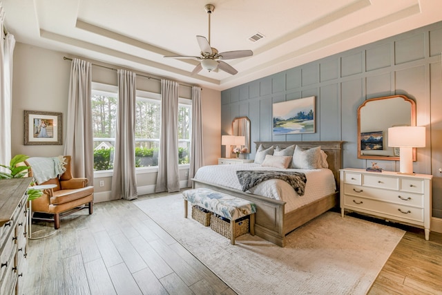 bedroom with ceiling fan, a raised ceiling, and light hardwood / wood-style floors