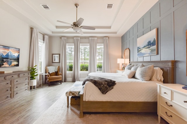 bedroom with ceiling fan, light hardwood / wood-style floors, and a tray ceiling