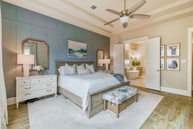 bedroom with connected bathroom, light hardwood / wood-style floors, a raised ceiling, and ceiling fan