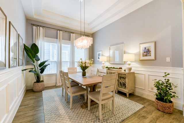 dining space featuring a raised ceiling, a notable chandelier, and light hardwood / wood-style flooring