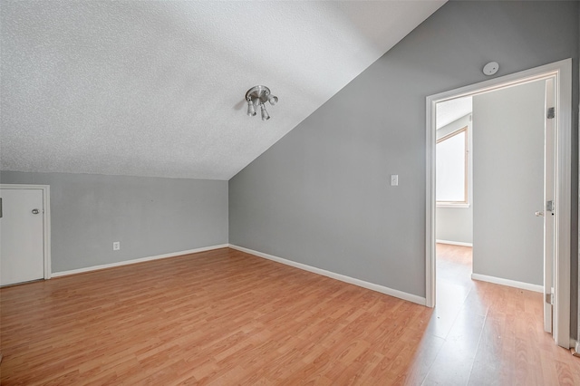 bonus room with lofted ceiling, light hardwood / wood-style floors, and a textured ceiling