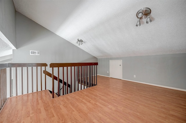 additional living space with wood-type flooring, lofted ceiling, and a textured ceiling