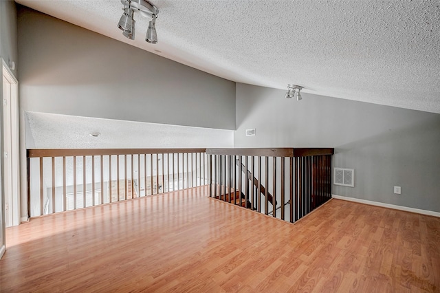 additional living space featuring lofted ceiling, hardwood / wood-style floors, and a textured ceiling