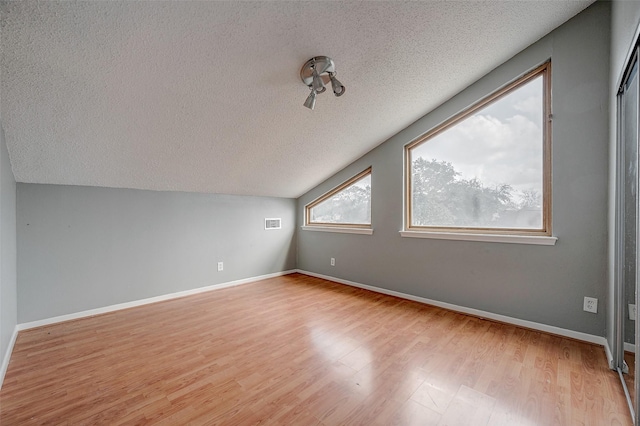 bonus room featuring lofted ceiling, a textured ceiling, and light wood-type flooring