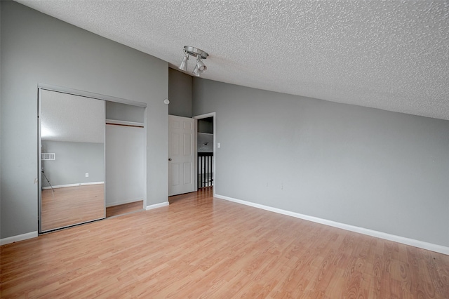 unfurnished bedroom featuring a closet, lofted ceiling, light hardwood / wood-style flooring, and a textured ceiling