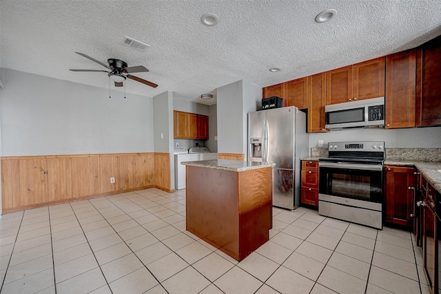 kitchen with light tile patterned floors, a kitchen island, stainless steel appliances, light stone countertops, and washer and clothes dryer