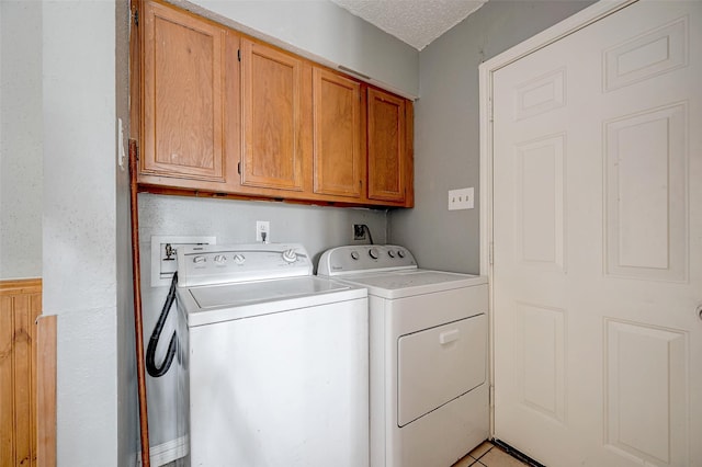 clothes washing area with cabinets, a textured ceiling, and washing machine and clothes dryer