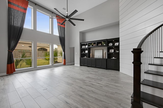 unfurnished living room with a high ceiling, ceiling fan, and light hardwood / wood-style floors