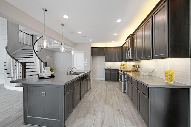 kitchen featuring appliances with stainless steel finishes, a kitchen island with sink, dark brown cabinets, and decorative light fixtures