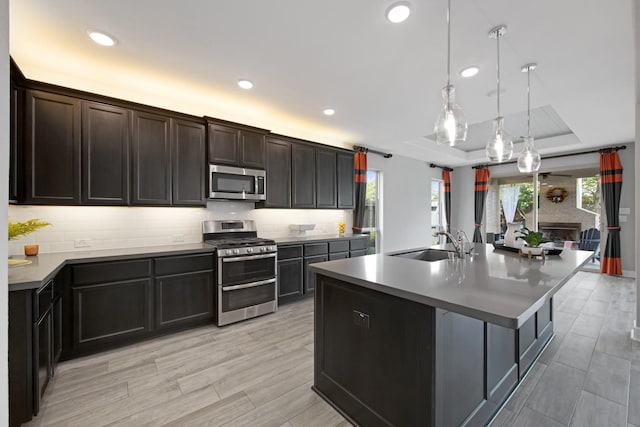 kitchen featuring pendant lighting, sink, appliances with stainless steel finishes, an island with sink, and a raised ceiling