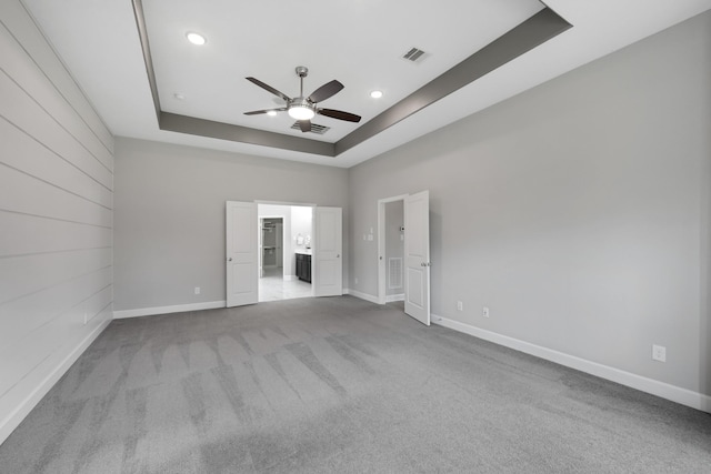 unfurnished bedroom with ceiling fan, light colored carpet, ensuite bathroom, and a tray ceiling