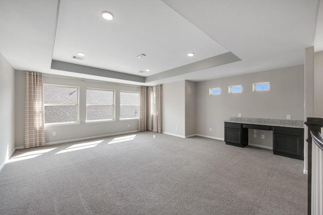 unfurnished living room featuring a raised ceiling, light carpet, and built in desk