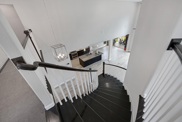 stairway with a high ceiling, hardwood / wood-style floors, and a notable chandelier