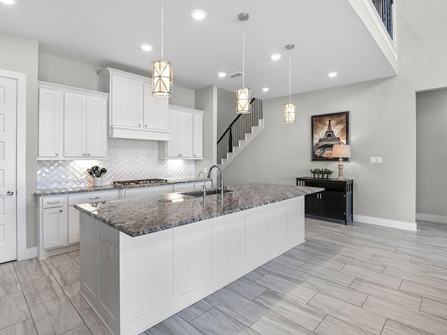 kitchen featuring pendant lighting, an island with sink, sink, white cabinets, and dark stone counters