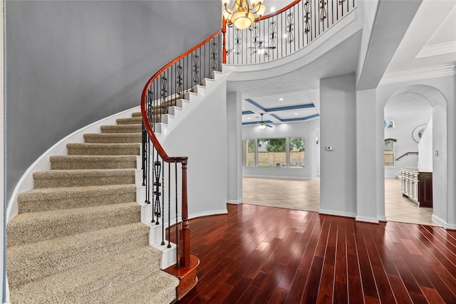 entryway with ceiling fan with notable chandelier, wood-type flooring, a high ceiling, ornamental molding, and coffered ceiling