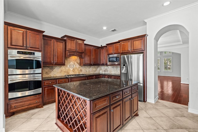 kitchen with stainless steel appliances, a center island, light tile patterned flooring, decorative backsplash, and dark stone counters