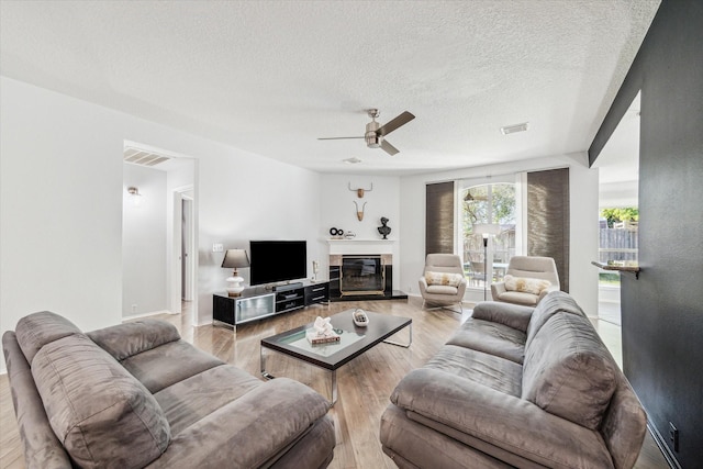 living room with ceiling fan, light hardwood / wood-style flooring, and a textured ceiling