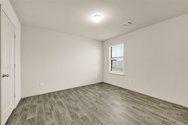 empty room with a textured ceiling, wood finished floors, and visible vents