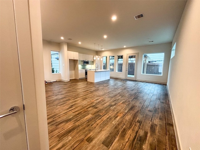 unfurnished living room with sink, plenty of natural light, and dark hardwood / wood-style floors