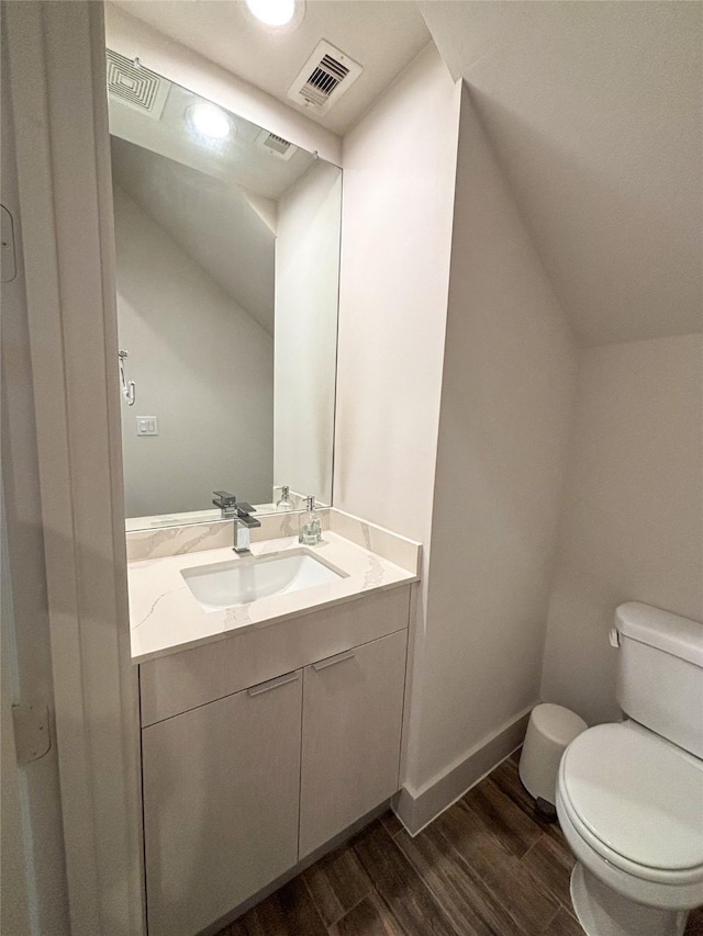 bathroom featuring wood-type flooring, vaulted ceiling, vanity, and toilet