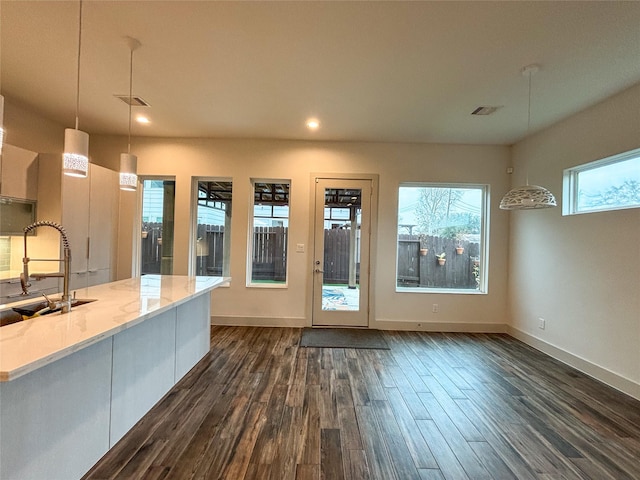 kitchen with sink, light stone counters, decorative light fixtures, plenty of natural light, and dark hardwood / wood-style flooring