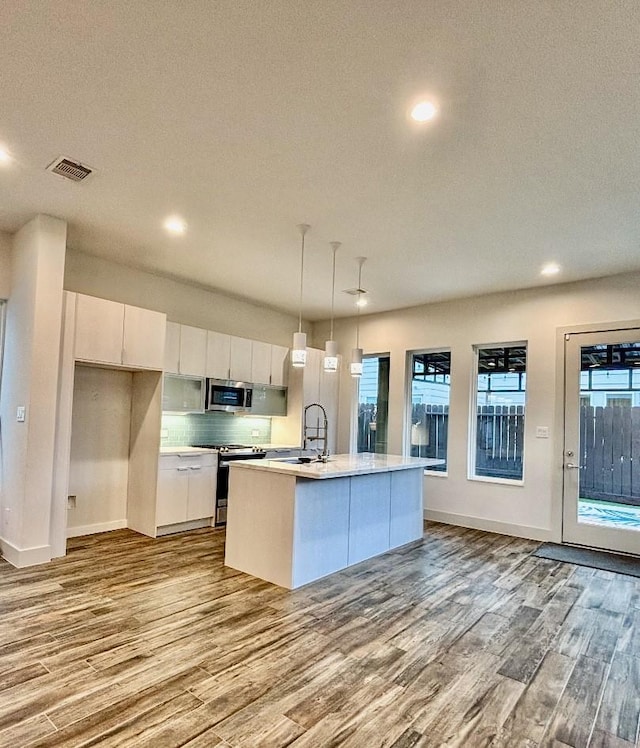 kitchen featuring light hardwood / wood-style flooring, white cabinetry, a kitchen island with sink, stainless steel appliances, and decorative light fixtures