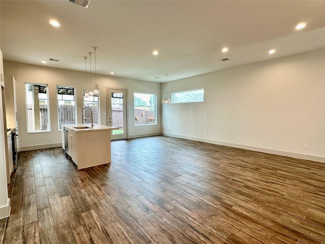 interior space with pendant lighting, sink, dark wood-type flooring, a center island with sink, and stainless steel dishwasher