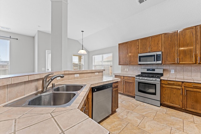 kitchen with sink, stainless steel appliances, decorative backsplash, decorative light fixtures, and tile countertops