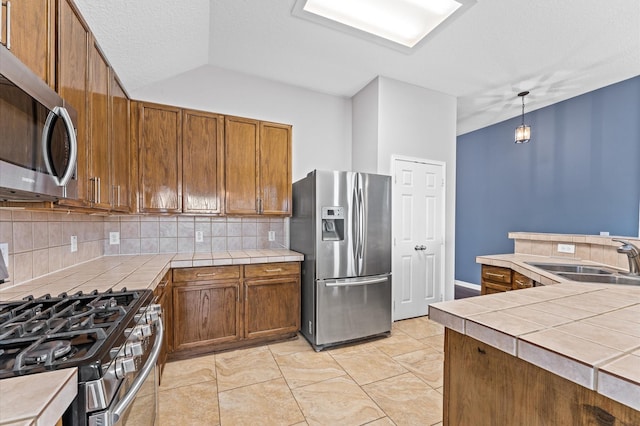 kitchen featuring vaulted ceiling, sink, decorative backsplash, hanging light fixtures, and stainless steel appliances