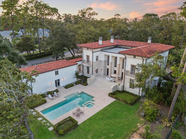 back house at dusk featuring a patio, a balcony, and a yard