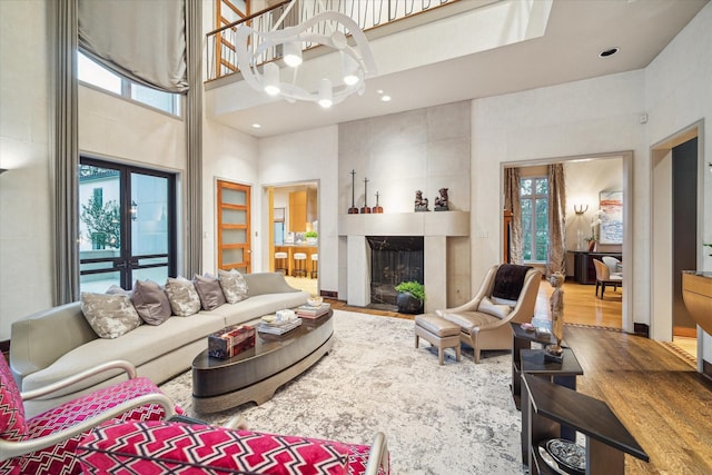 living room with a notable chandelier, a tiled fireplace, hardwood / wood-style floors, and a high ceiling