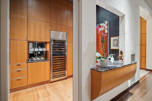 interior space featuring dark stone countertops, wine cooler, and light hardwood / wood-style flooring