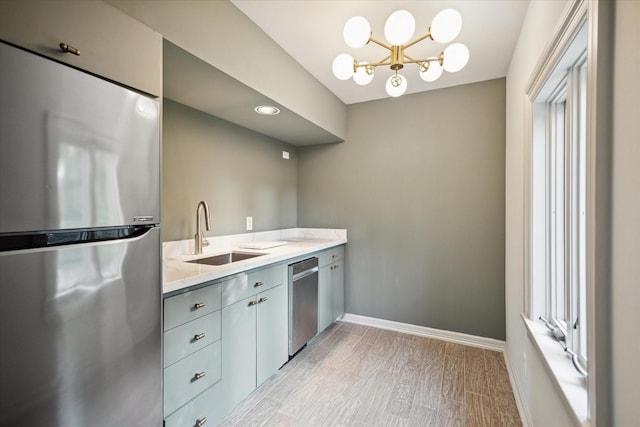 kitchen featuring sink, light stone counters, a chandelier, stainless steel appliances, and light hardwood / wood-style floors