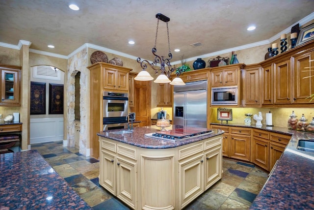 kitchen featuring sink, hanging light fixtures, built in appliances, ornamental molding, and an island with sink