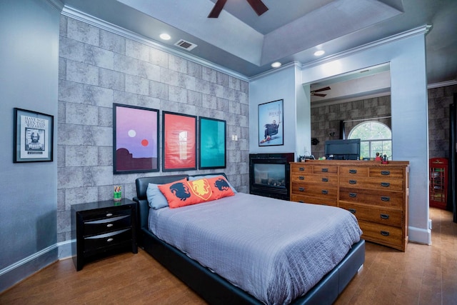 bedroom with ceiling fan, ornamental molding, a tray ceiling, and wood-type flooring