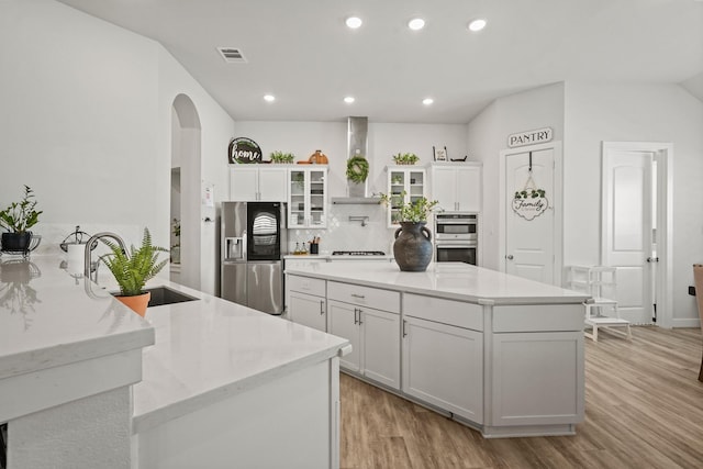 kitchen with white cabinets, stainless steel appliances, sink, and wall chimney range hood