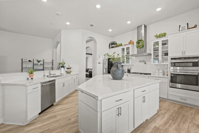 kitchen with sink, stainless steel appliances, a center island, white cabinets, and wall chimney exhaust hood